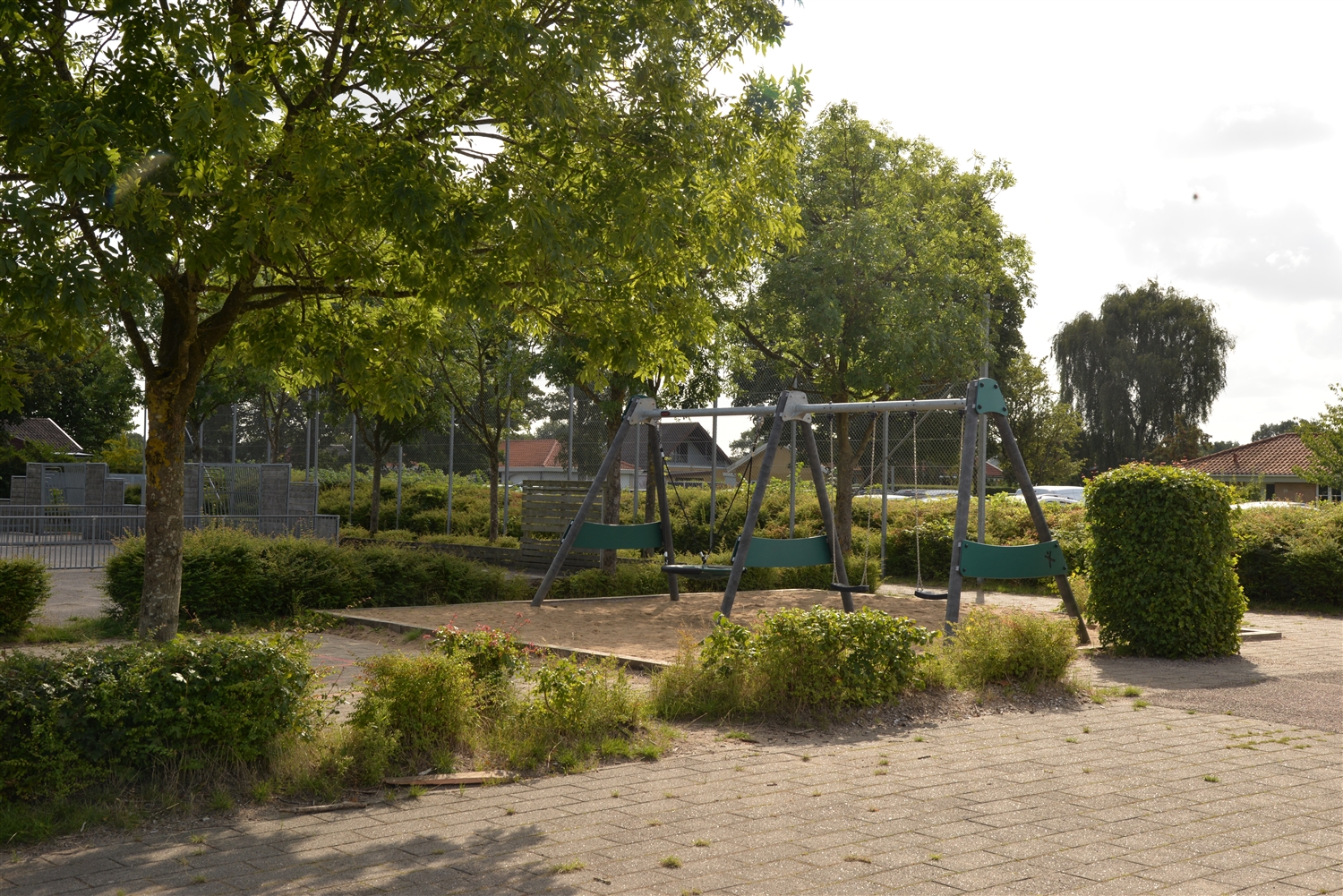 Legeplads med grønne træer og buske samt et gyngestativ.
