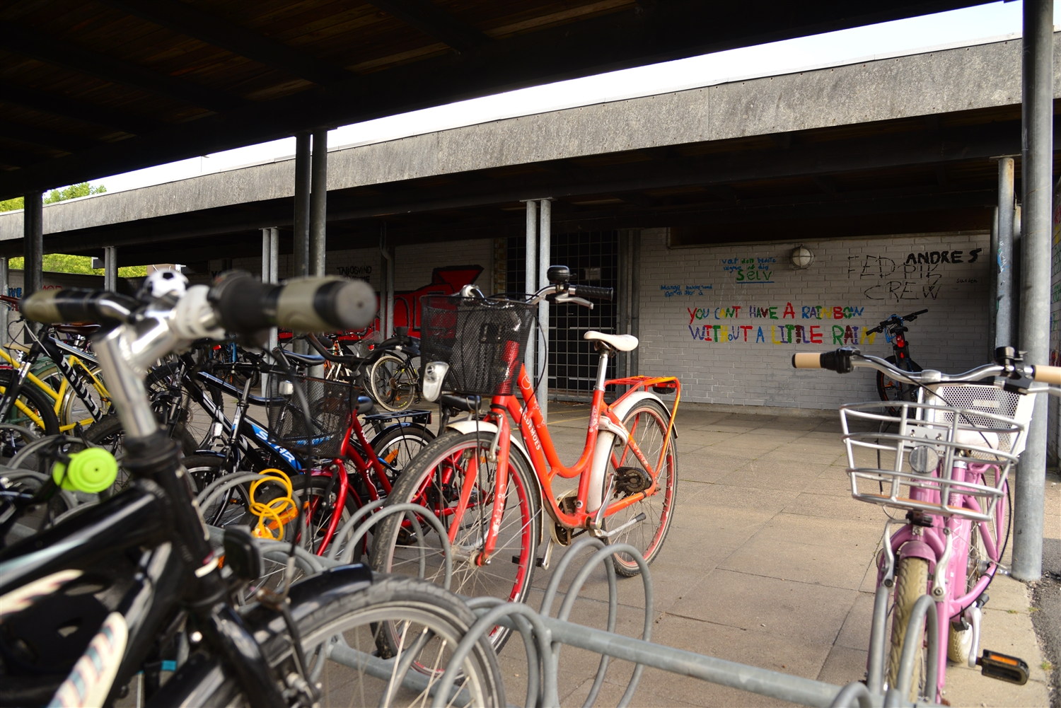 Et cykelskur, hvor der i forgrunden er en masse cykler. I baggrunden ses en mur med forskelligt graffiti på.  